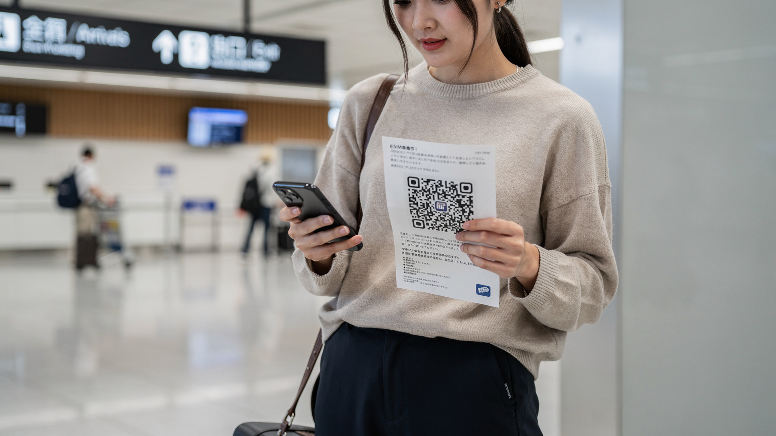Một du khách trẻ đang dùng điện thoại để quét mã QR kích hoạt eSIM trong sảnh chờ sân bay Haneda, với các biển hiệu bằng tiếng Nhật phía sau.
