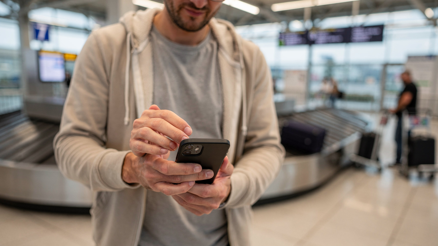 Ein Reisender am Flughafen Berlin Brandenburg (BER) nutzt sein Smartphone, um eine eSIM zu aktivieren und seine Reiseroute zu überprüfen, während er auf sein Gepäck wartet.