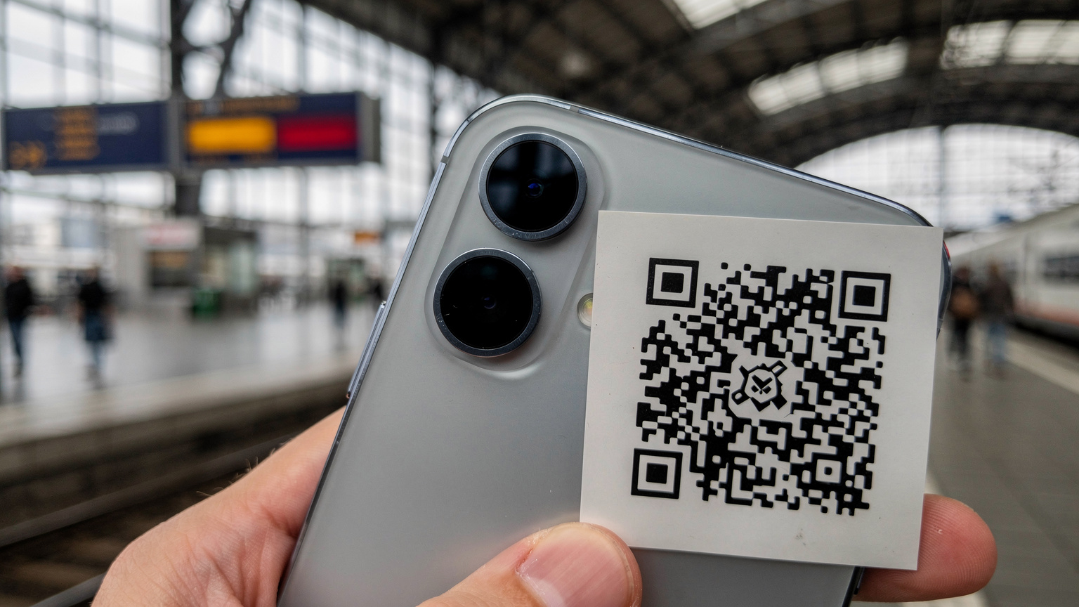 Eine Nahaufnahme eines Smartphones, das einen QR-Code scannt, der für die eSIM-Aktivierung benötigt wird. Im Hintergrund ist ein geschäftiger deutscher Bahnhof wie der Berliner Hauptbahnhof zu erkennen.
