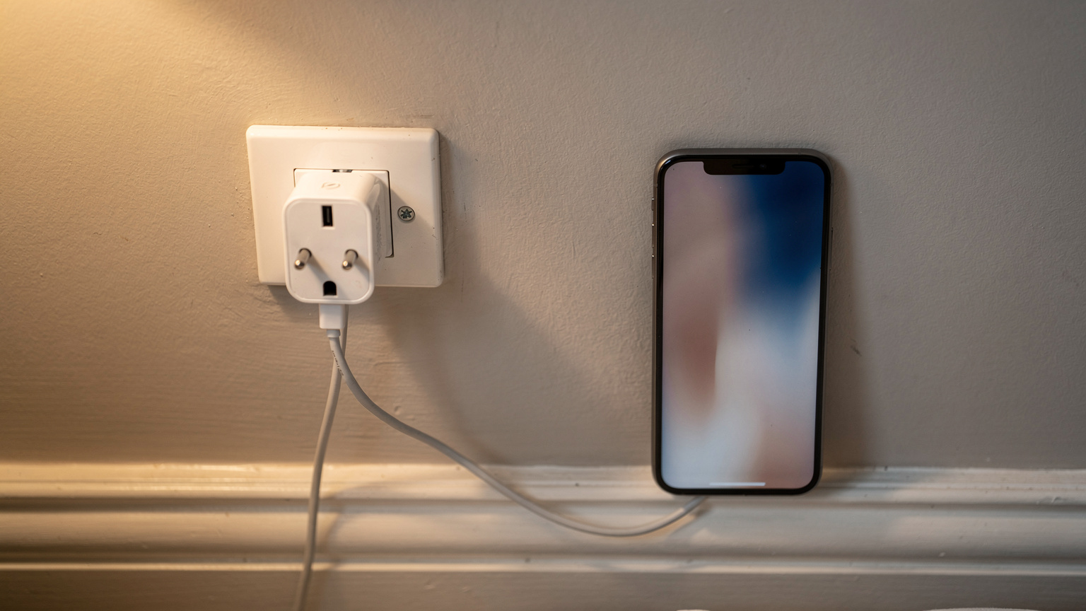 Ein britischer Typ-G-Reiseadapter steckt in einer Steckdose, daneben liegt ein Smartphone, das ein Ladekabel angeschlossen hat und eine eSIM-Einrichtungsanleitung anzeigt.