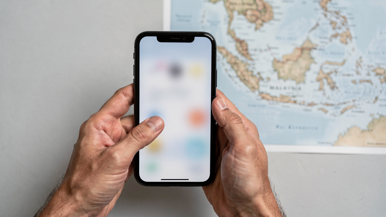 Pandangan dekat tangan seorang individu sedang menyentuh skrin telefon pintar, menunjukkan proses pemilihan dan pengaktifan pelan eSIM dengan latar belakang peta digital Malaysia yang kabur.
