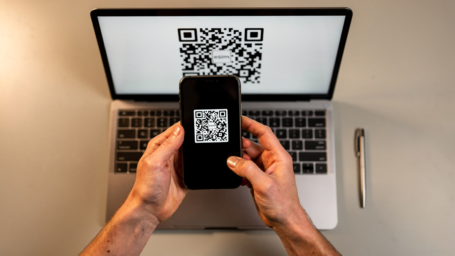 Nahaufnahme eines Smartphones, das einen QR-Code auf einem Laptop-Bildschirm scannt, um eine eSIM zu aktivieren, mit Händen, die das Telefon halten.