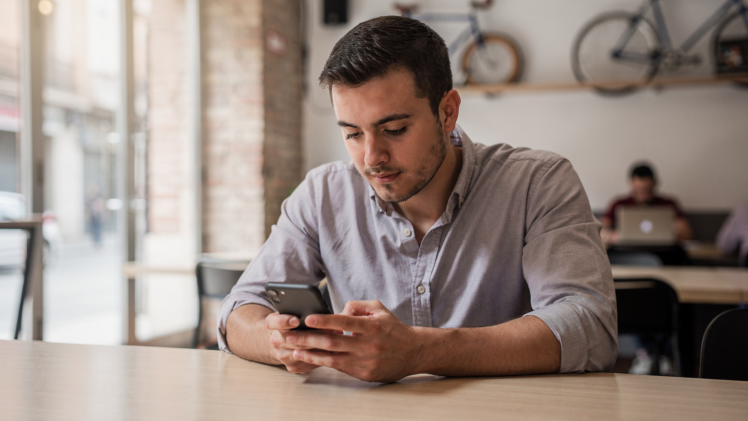 Una persona concentrada revisando su teléfono en un café moderno y luminoso, símbolo de la conectividad que la eSIM permite.