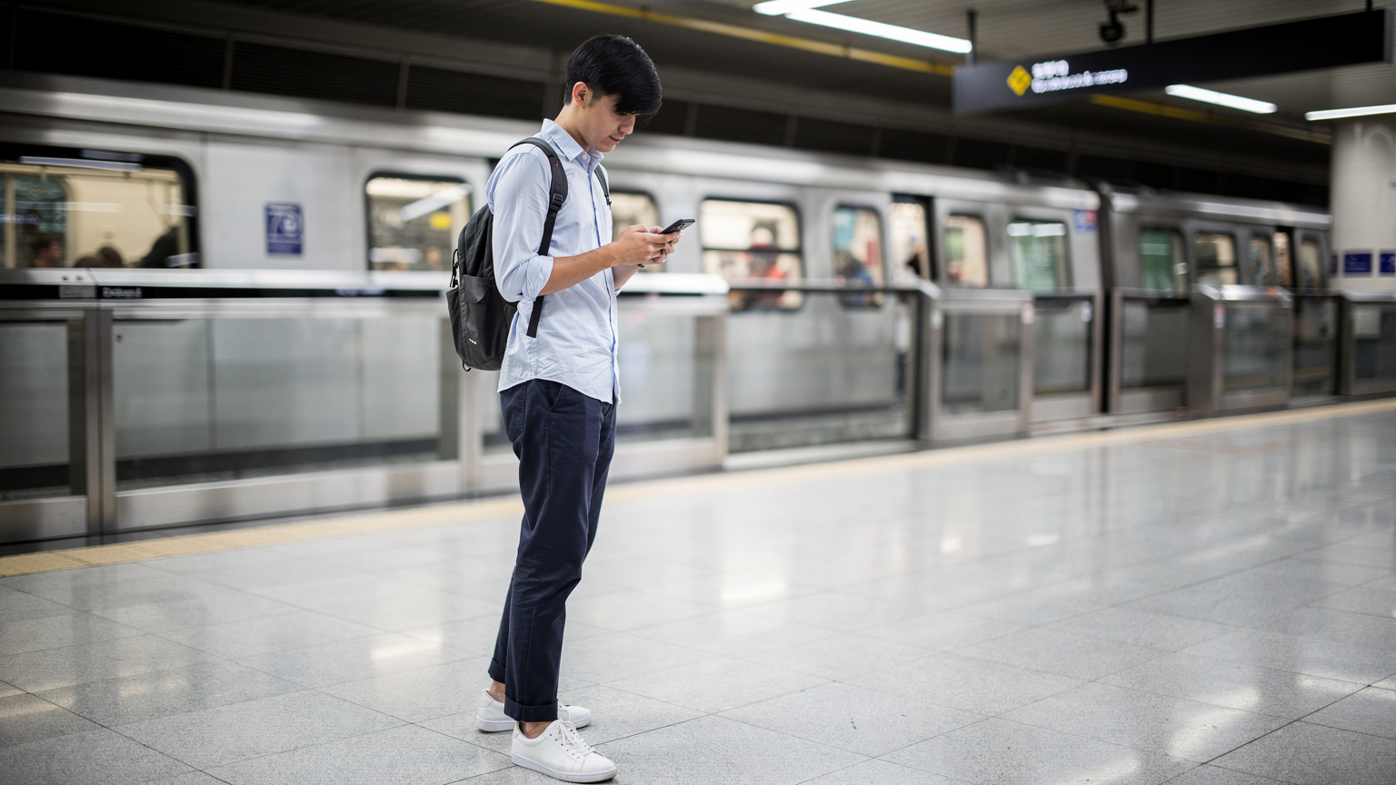 Seorang pria memegang ponsel di stasiun MRT bawah tanah di Singapura, menunjukkan betapa mudahnya tetap terhubung di kota modern ini.