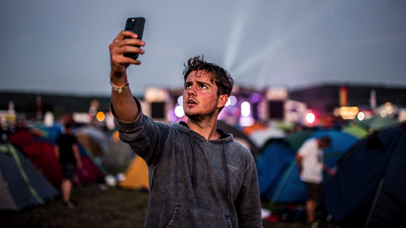 Ein Festivalbesucher versucht verzweifelt, auf seinem Smartphone Empfang zu finden, während das Signal schwach ist.