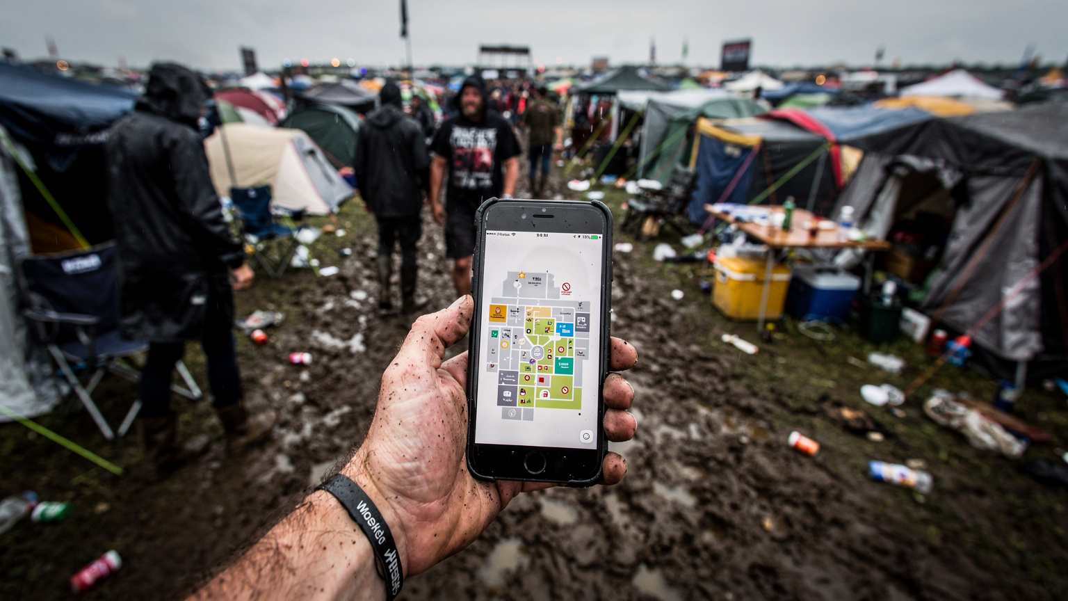 Eine Person hält ein Smartphone in einem überfüllten Zeltbereich eines Festivals, der Bildschirm zeigt eine Karte oder einen Fahrplan.
