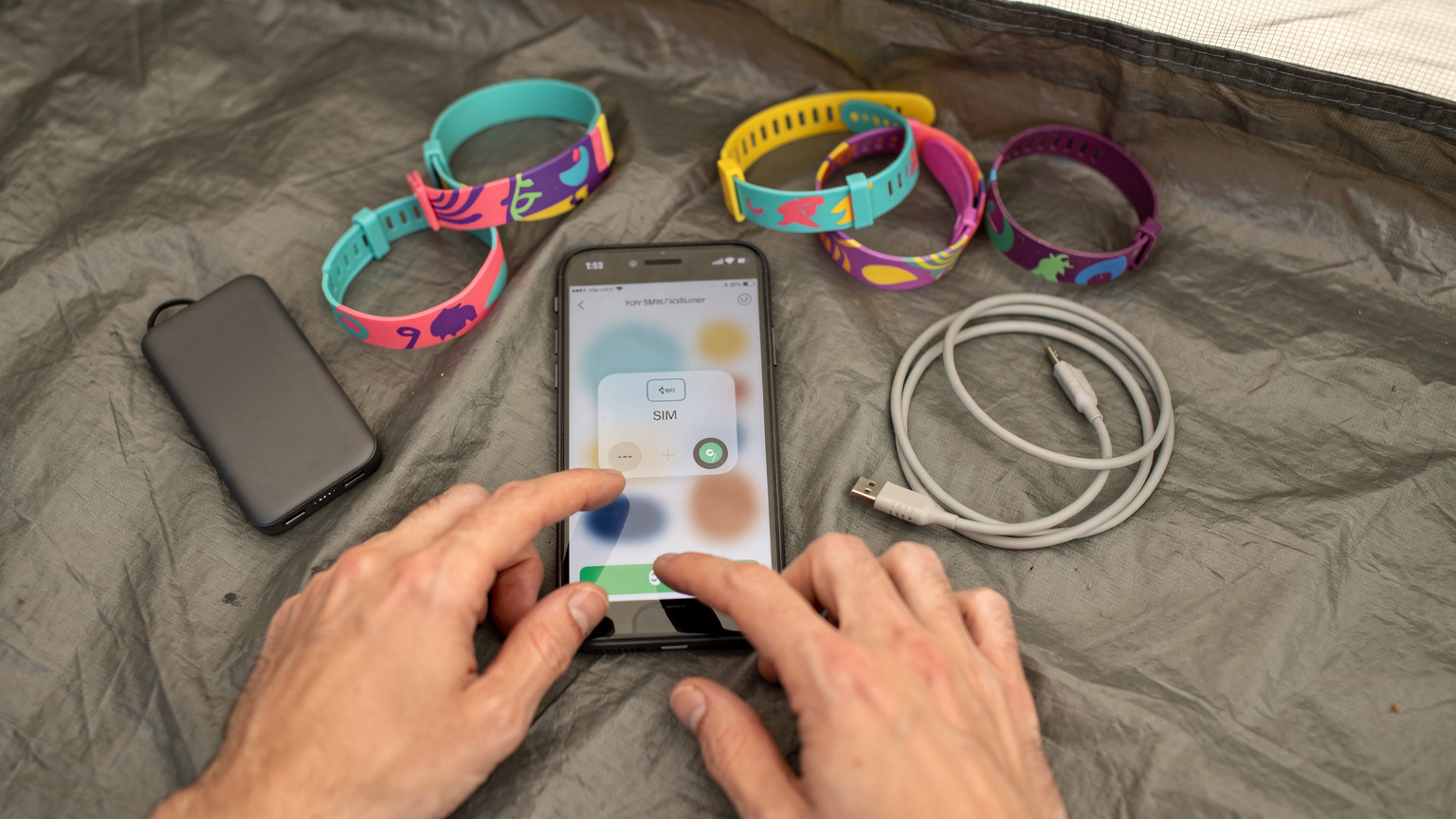 Nahaufnahme eines Smartphones mit einer eSIM-Profil-Installationsseite, umgeben von Festivalbändchen und einer Powerbank auf einem Zeltboden.