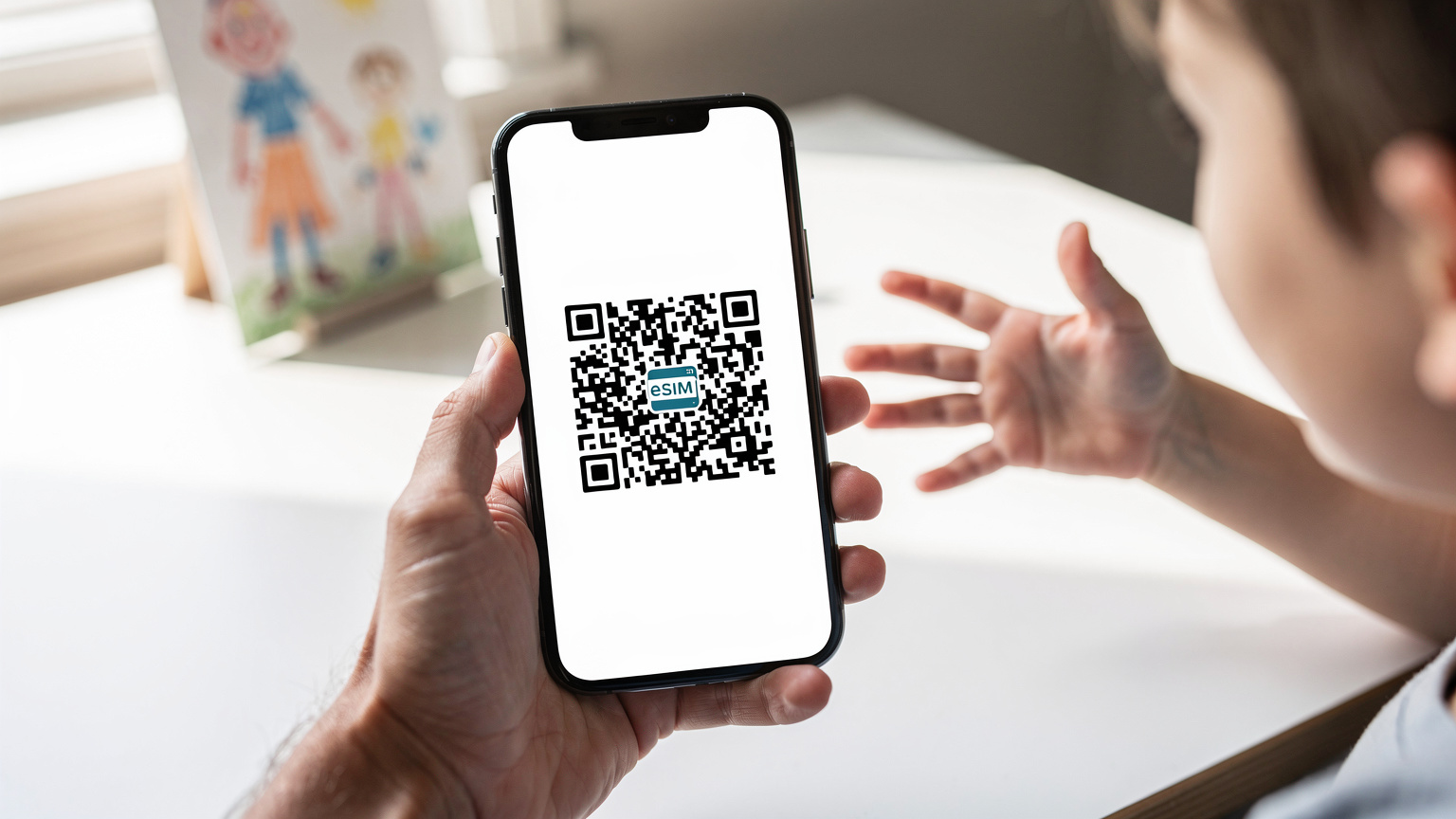 A close-up shot of a smartphone screen showing an eSIM activation QR code, held by a parent's hand, with a child's hand reaching playfully towards it in the background.