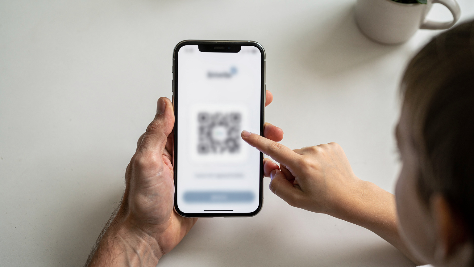 Manos de un adulto sosteniendo un smartphone, mostrando la pantalla de configuración de una eSIM con un código QR escaneado, mientras una mano infantil curiosa señala la pantalla.