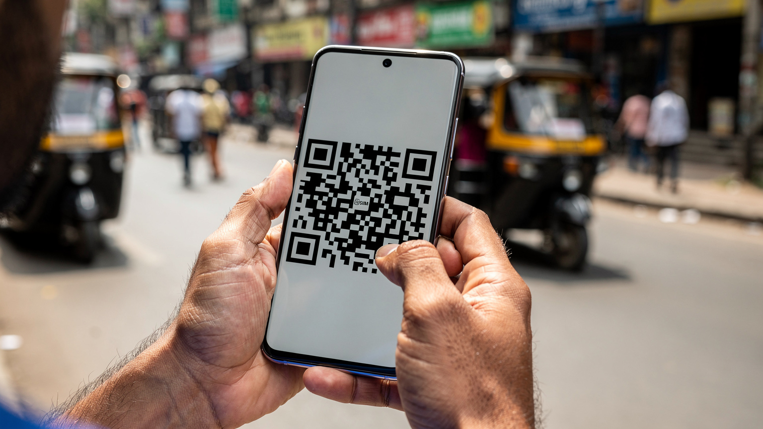 एक व्यक्ति अपने Samsung Galaxy S27 पर eSIM के लिए QR कोड स्कैन कर रहा है, पृष्ठभूमि में मुंबई की एक व्यस्त सड़क दिख रही है.