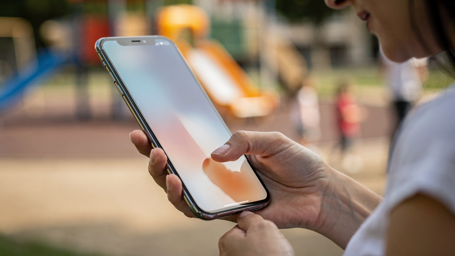 Bir annenin eli, akıllı telefonunda Cellesim uygulamasından farklı eSIM veri planlarını inceliyor, arka planda bulanık bir çocuk parkı görünüyor.