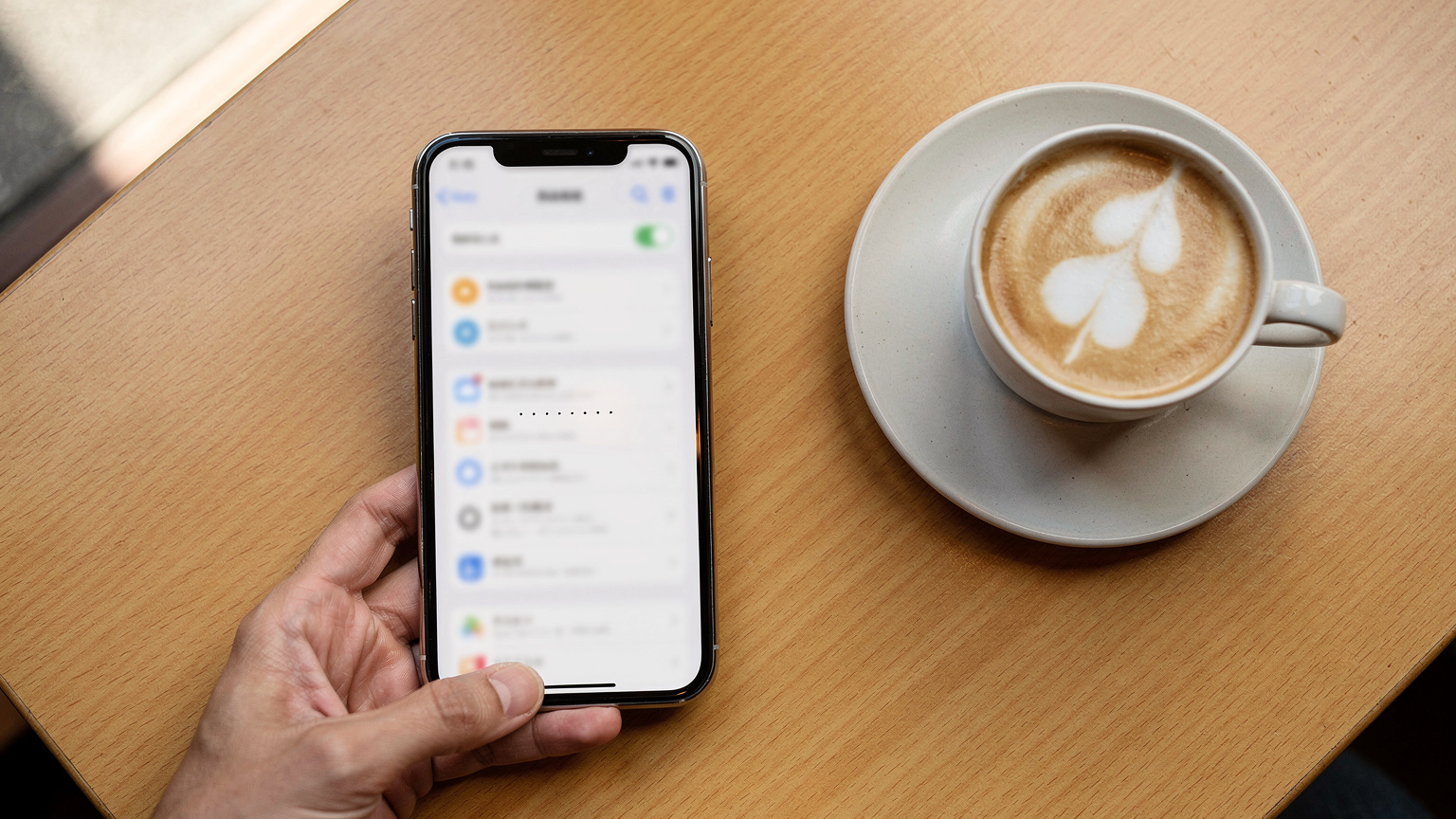 iPhoneの設定画面でEIDを確認し、eSIMの対応状況をチェックする様子。手元のコーヒーカップが日本のカフェの雰囲気を醸し出す。