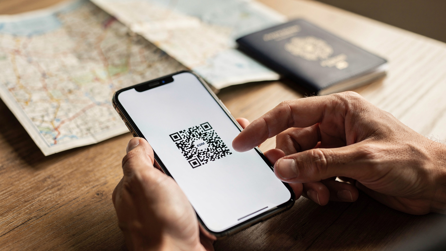 A close-up shot of a traveler's hands gently tapping on a smartphone screen, displaying a clear eSIM activation QR code, with a blurred map in the background.