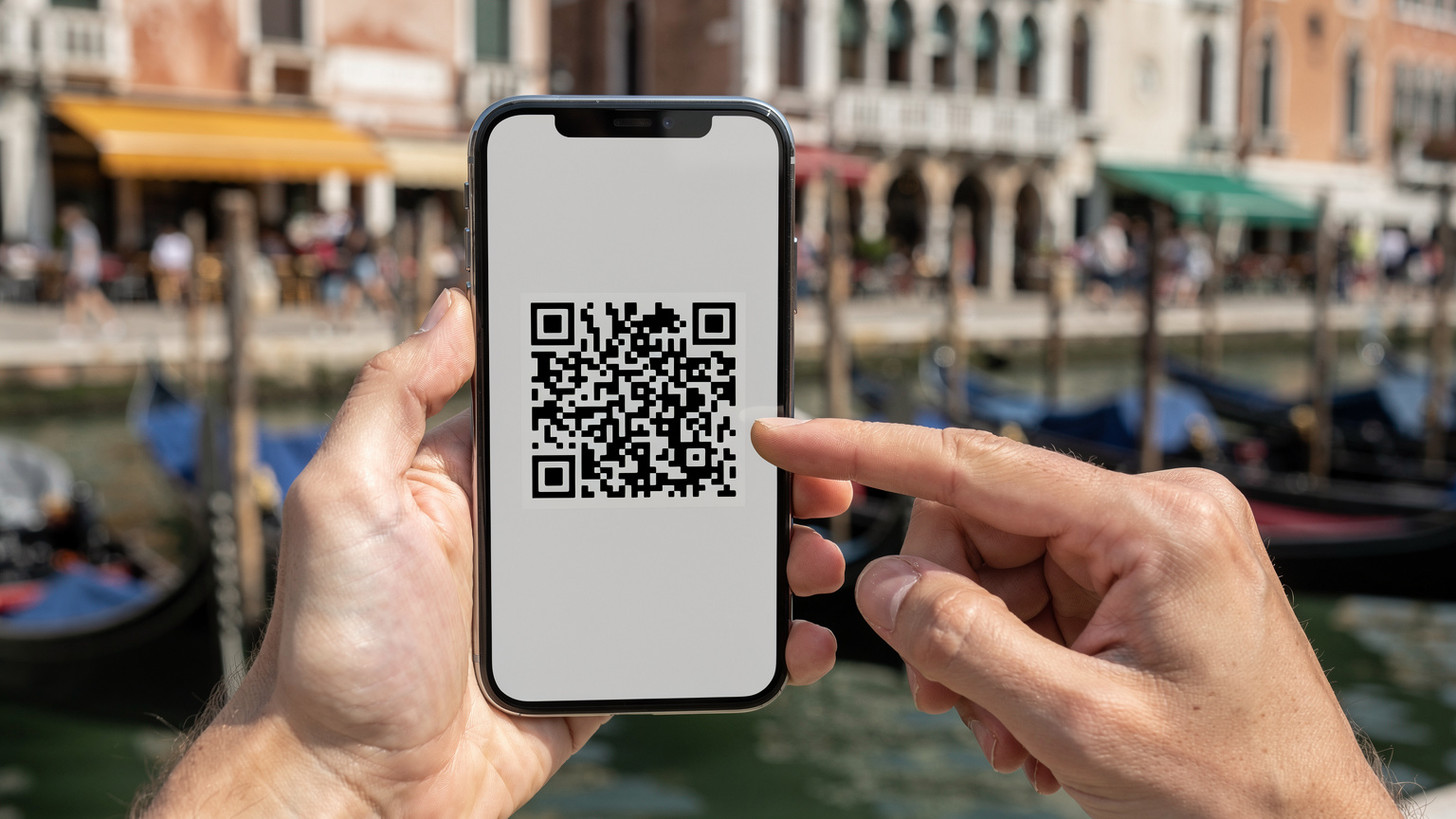 Nahaufnahme eines Smartphones, das einen QR-Code für die eSIM-Installation anzeigt, gehalten von Händen vor dem Hintergrund einer belebten Hafenpromenade in Venedig.