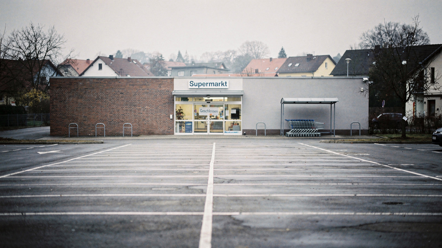Ein verlassener Supermarktparkplatz an einem Sonntagnachmittag in einer kleinen deutschen Stadt, mit einem "Geschlossen"-Schild an der Tür.