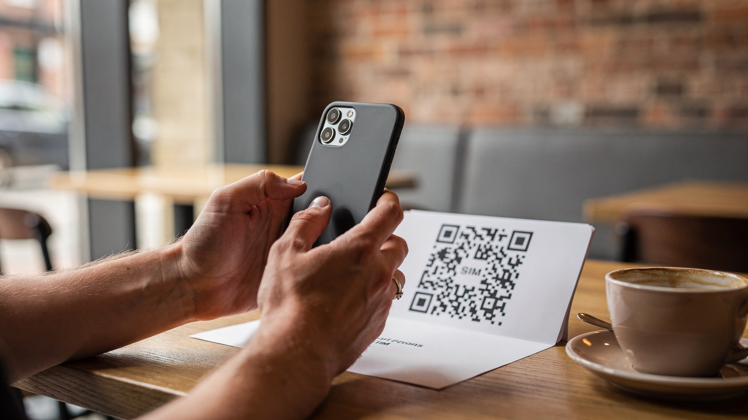 Birleşik Krallık'ta bir kafede, bir elinde akıllı telefon tutan bir kişi, diğer eliyle bir QR kodunu tarayarak eSIM kurulumunu tamamlıyor.