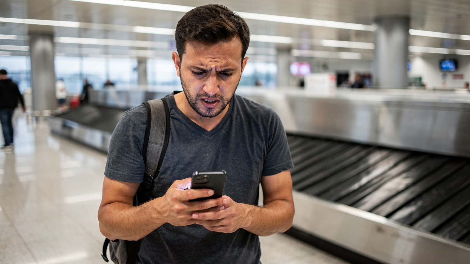 İstanbul Havalimanı'nda, bagaj bantlarının yanında duran bir gezgin, yorgun bir ifadeyle telefonunun ekranına bakıyor, muhtemelen ağ bağlantısı sorunu yaşıyor.