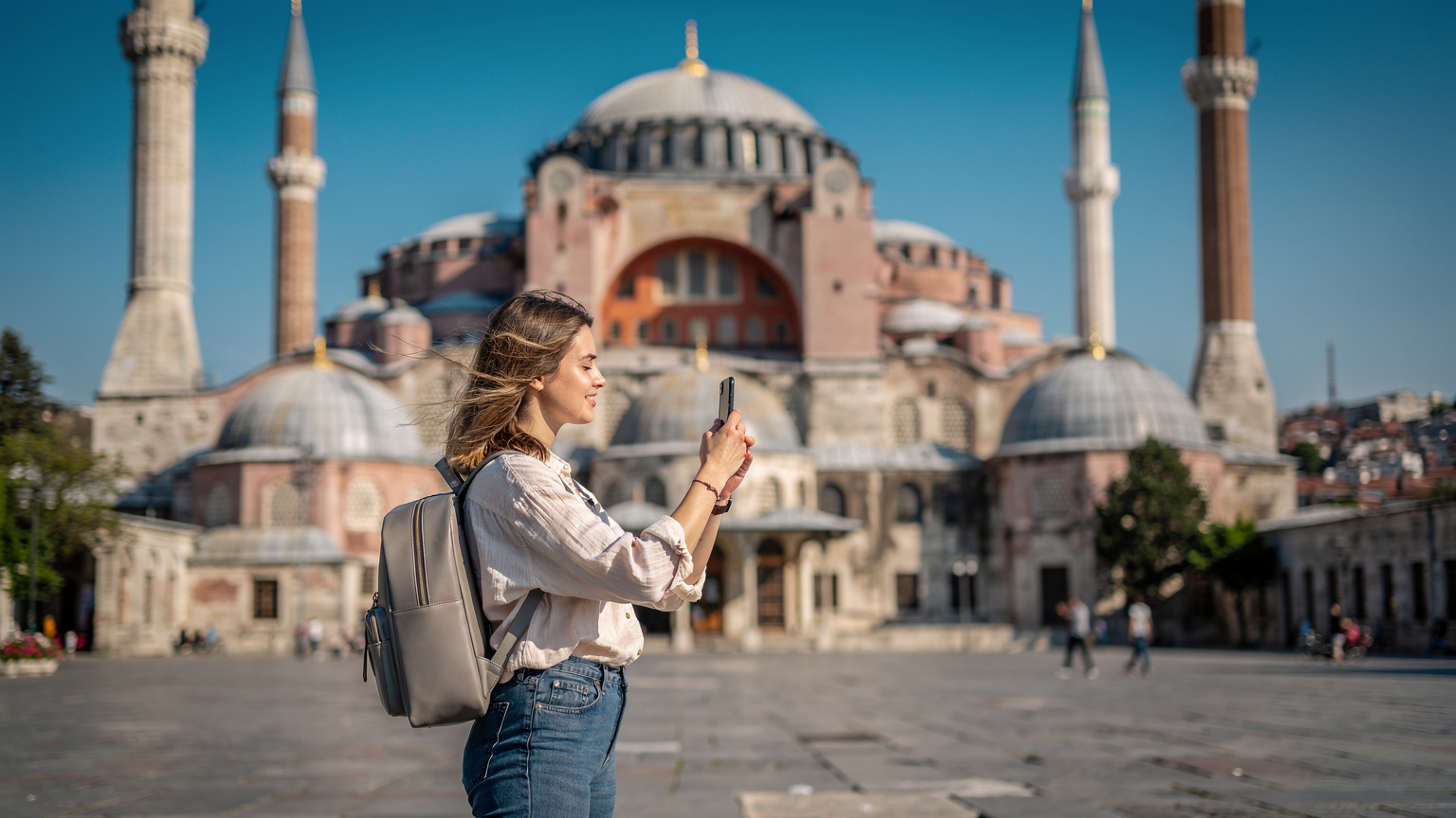 Ayasofya'nın ihtişamlı silüeti önünde, genç bir turist elindeki telefonuyla video çekimi yapıyor, arka planda tarihi yarımada manzarası uzanıyor.