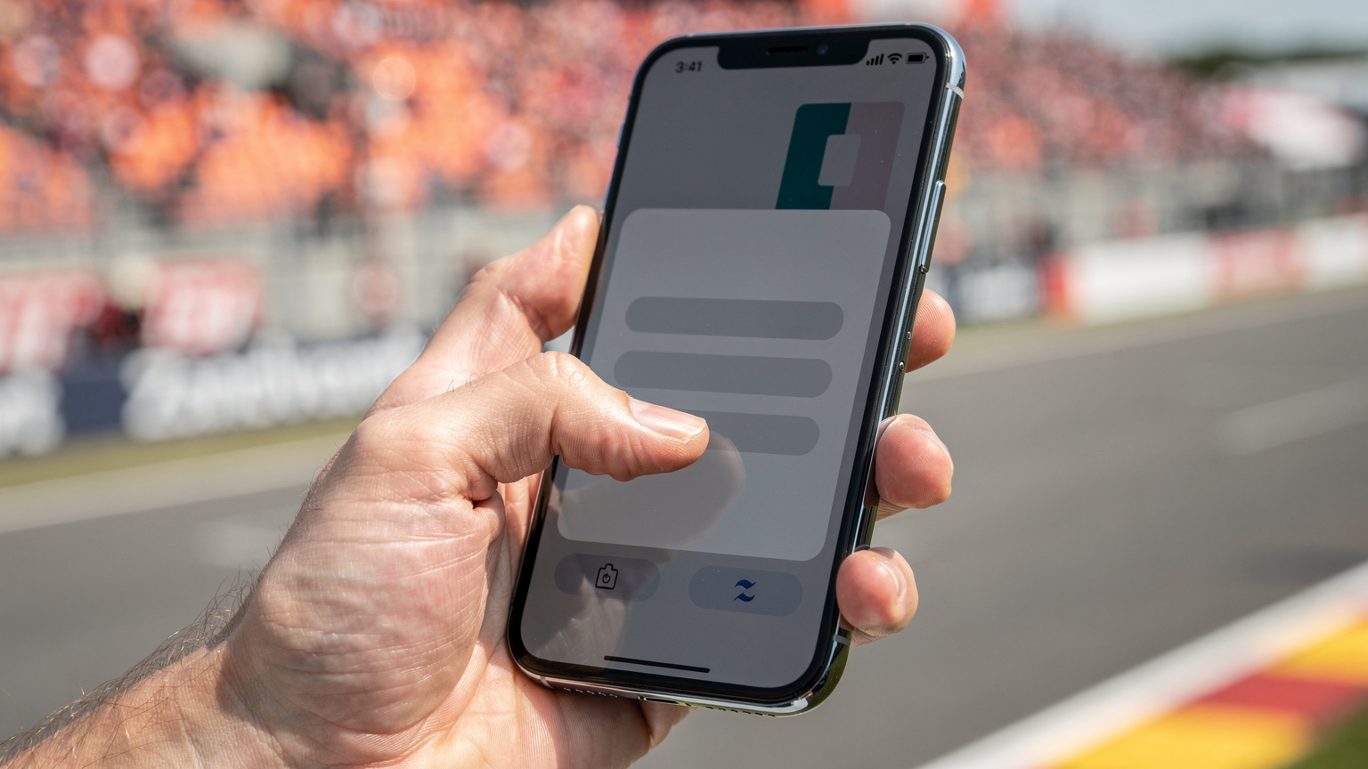 Een close-up van een volwassen hand die een smartphone vasthoudt, met de focus op het scherm waar een eSIM-installatieproces wordt getoond, op de achtergrond een onscherpe afbeelding van het Formule 1 circuit.