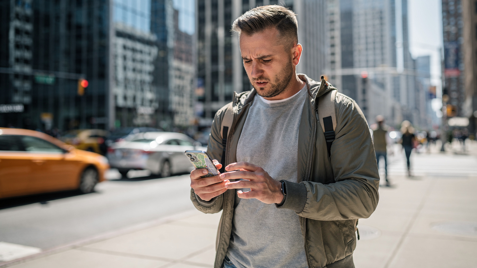 Un hombre usando su Samsung Galaxy S26 para navegar en un mapa digital, con rascacielos y tráfico de una ciudad estadounidense al fondo, durante el día.