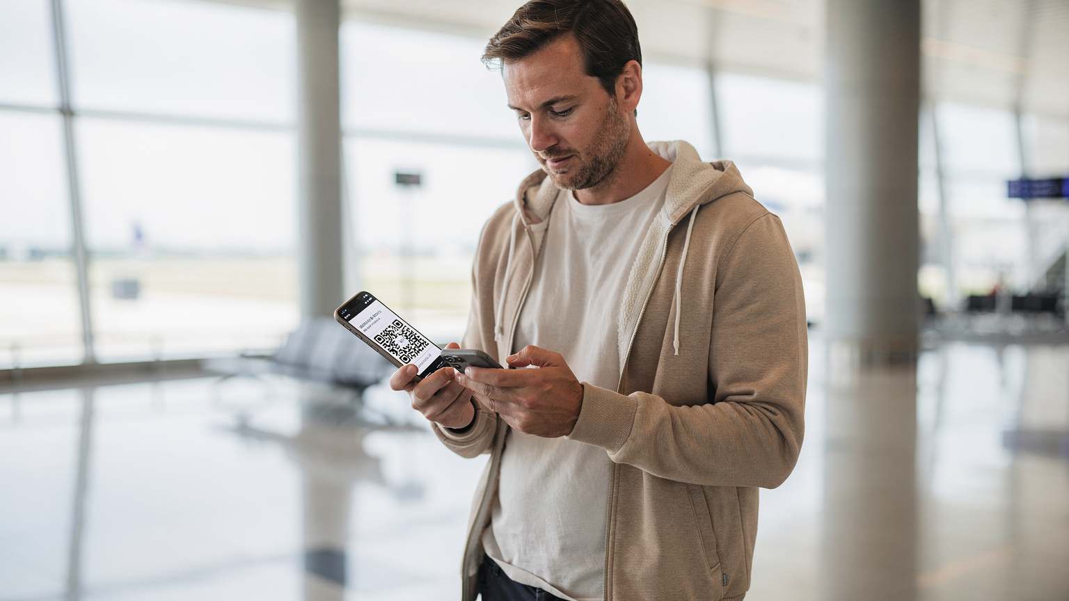 A traveler in a bright airport terminal, holding a smartphone and scanning an eSIM QR code, with a sense of ease and readiness for their flight.