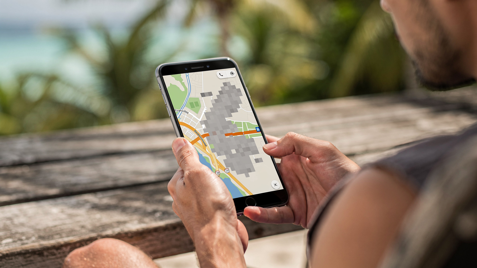 A close-up of a person's hands holding a smartphone displaying a partially loaded map, hinting at intermittent data signal on a tropical island.