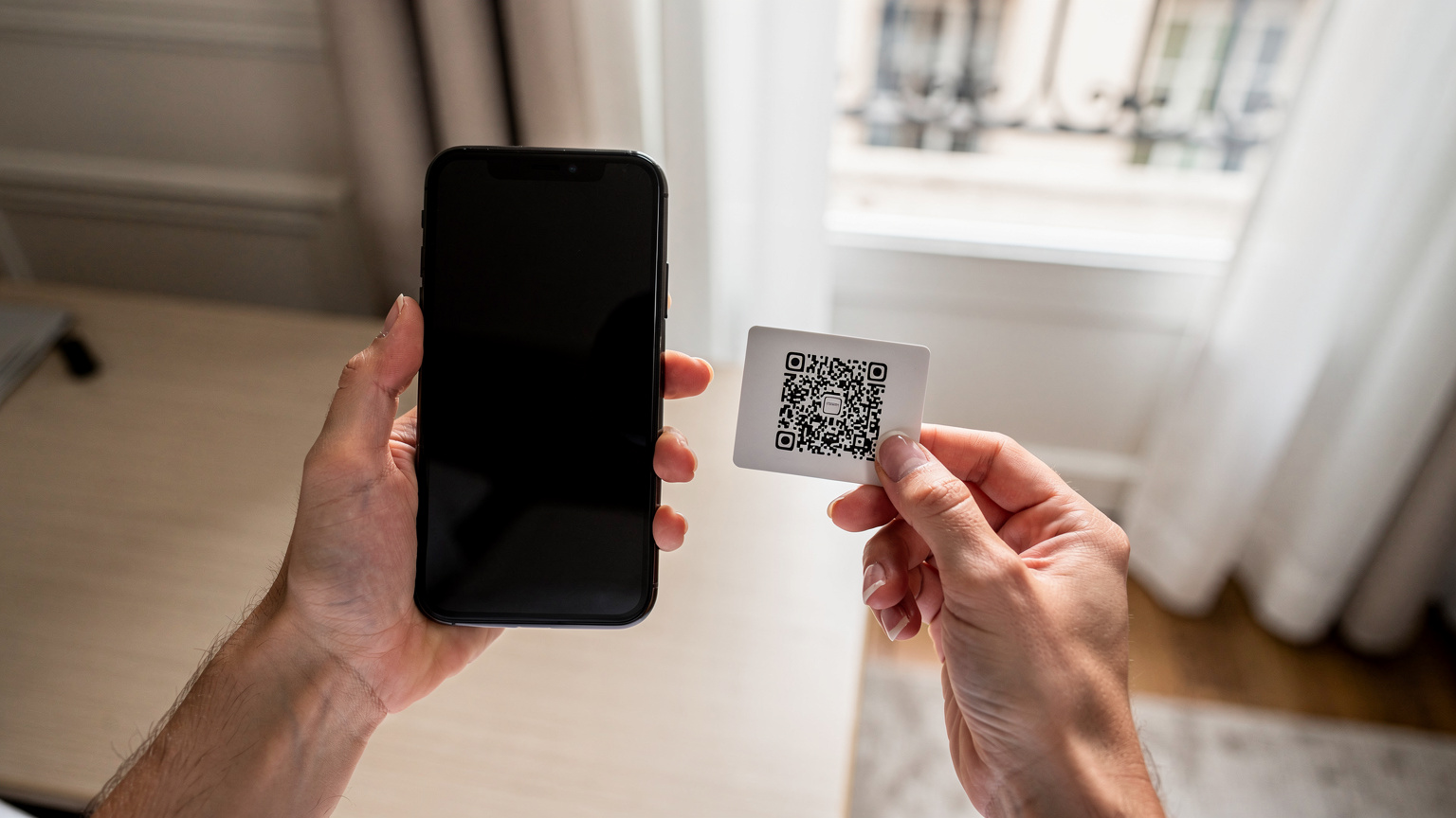 Ένα άτομο κρατά ένα smartphone και ένα χαρτί με QR code, ετοιμάζοντας να σαρώσει τον κωδικό για την εγκατάσταση μιας eSIM σε ένα φωτεινό, μοντέρνο δωμάτιο ξενοδοχείου.