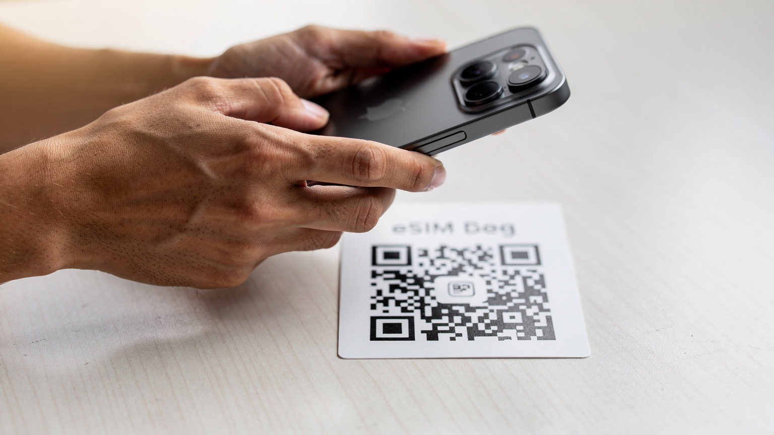 Nahaufnahme von Händen, die ein iPhone 18 halten, während sie einen QR-Code für die eSIM-Aktivierung scannen, mit einer minimalistischen, sauberen Tischplatte im Hintergrund, was den einfachen und schnellen Prozess unterstreicht.