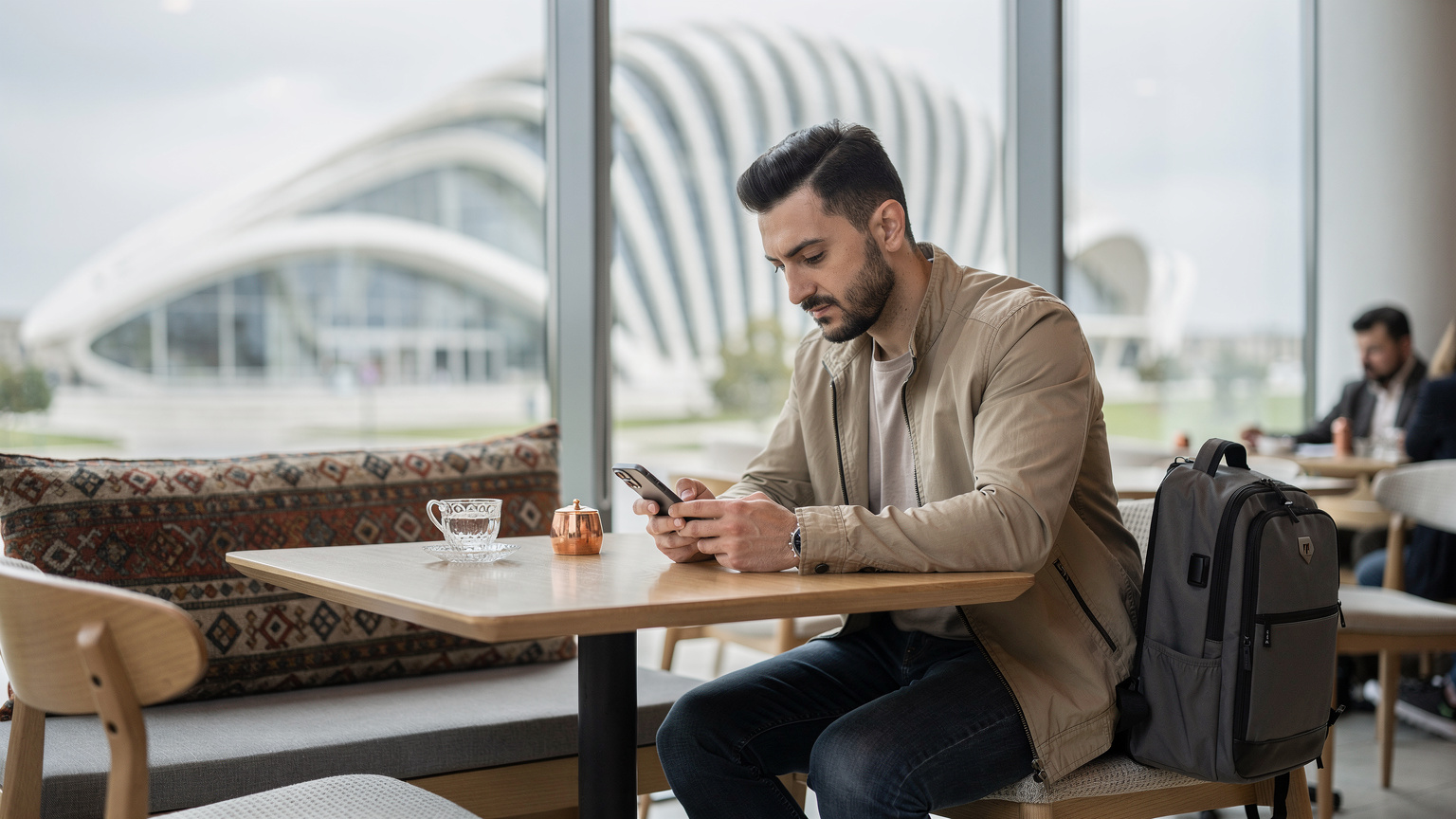 Ein Reisender vergleicht auf seinem Smartphone verschiedene eSIM-Tarife für Aserbaidschan, während er in einem Café in der Nähe des Heydar Aliyev Centers in Baku sitzt.