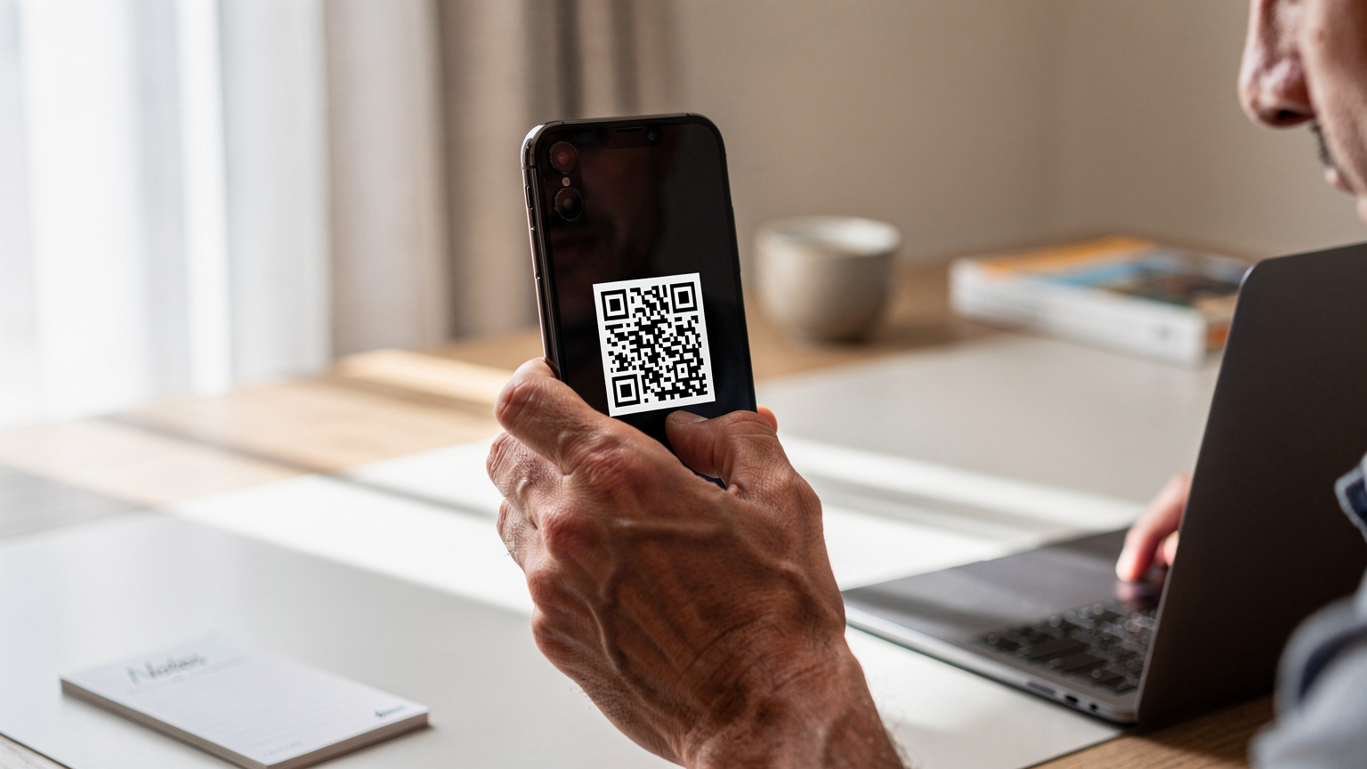 Detailní záběr rukou dospělého člověka, který na smartphonu s iOS skenuje QR kód pro aktivaci eSIM.