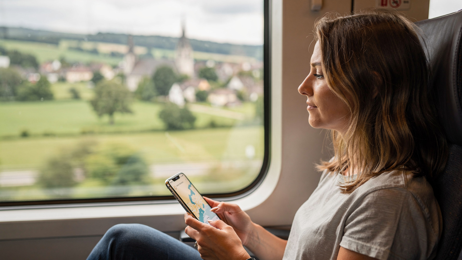 Avrupa'da seyahat ederken tren penceresinden dışarı bakarken elinde cep telefonu tutan bir kadın.