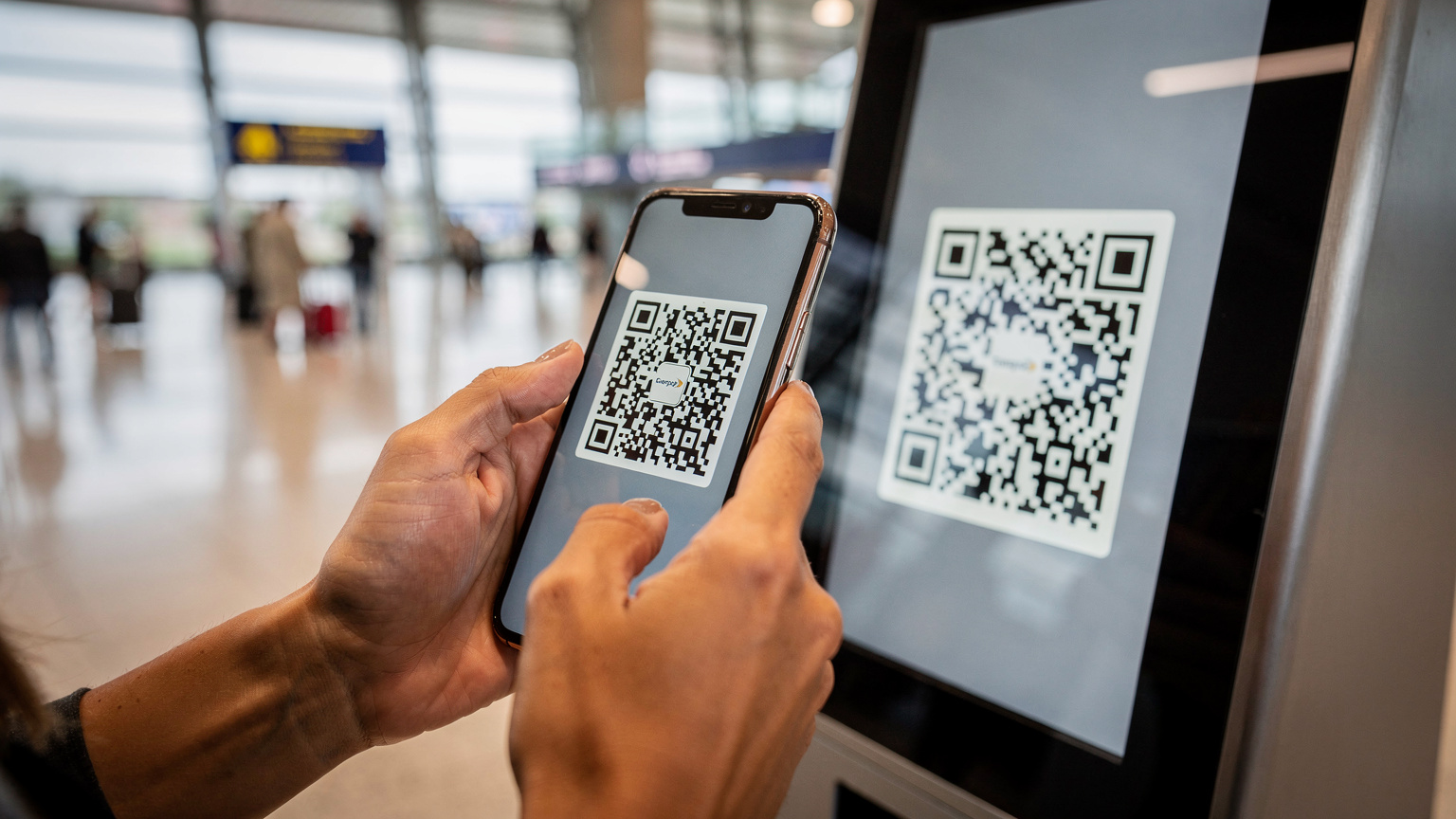 Een reiziger op het vliegveld scant een QR-code op een scherm met haar smartphone om een eSIM te activeren.