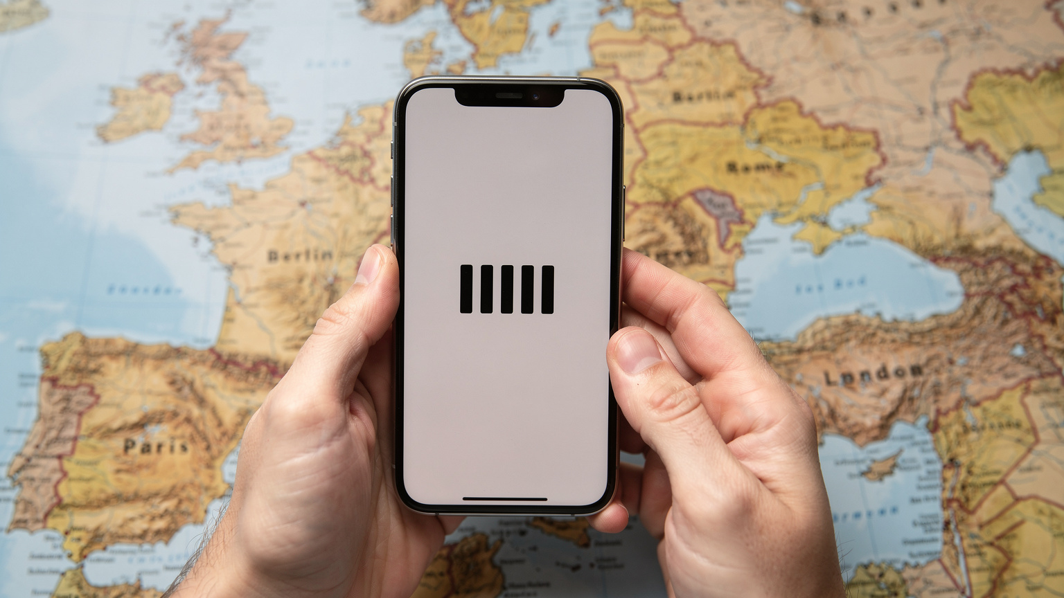 Manos de un viajero sosteniendo un teléfono mostrando una señal de red fuerte, con un mapa de Europa difuminado de fondo.