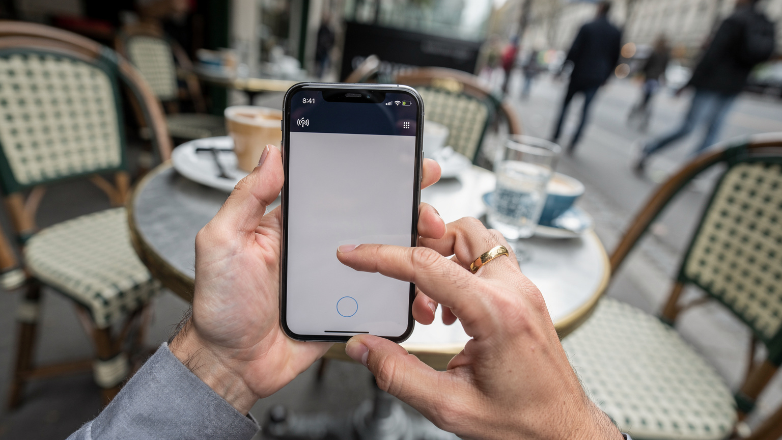A close-up of a parent's hands setting up a mobile hotspot on a smartphone, with a blurred background of a Parisian café terrace, emphasizing practical tech use on the go.