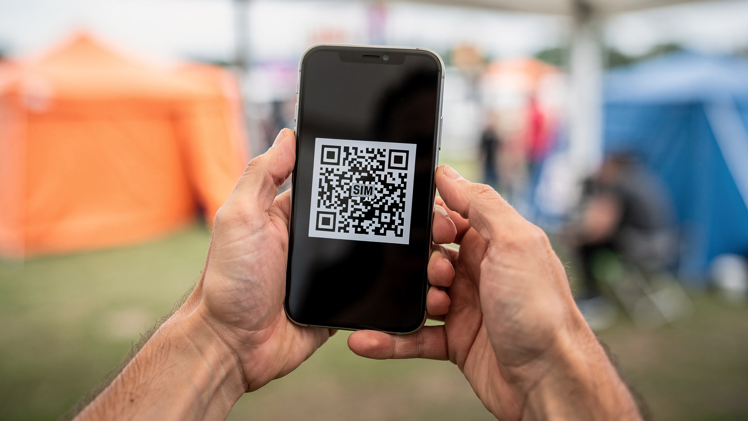 En mobilbruger scanner en QR-kode på en smartphone for at aktivere et eSIM, med festivalpladsen sløret i baggrunden, der understreger den digitale forberedelse.