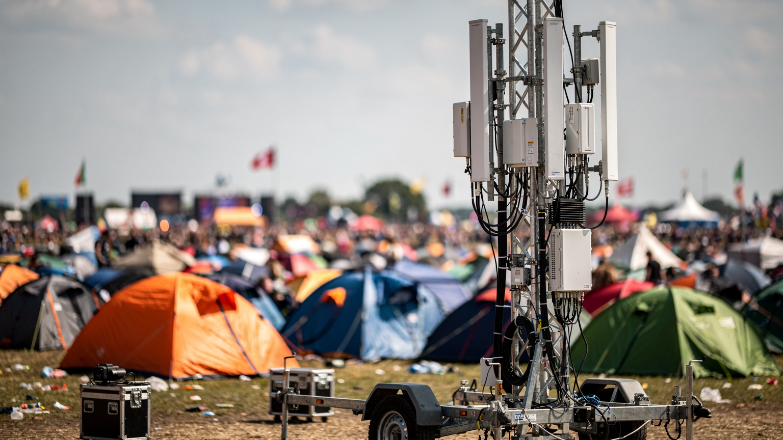 En mobilmast med adskillige antenner i et tæt befolket festivalområde viser den infrastrukturelle indsats for at opretholde forbindelse.