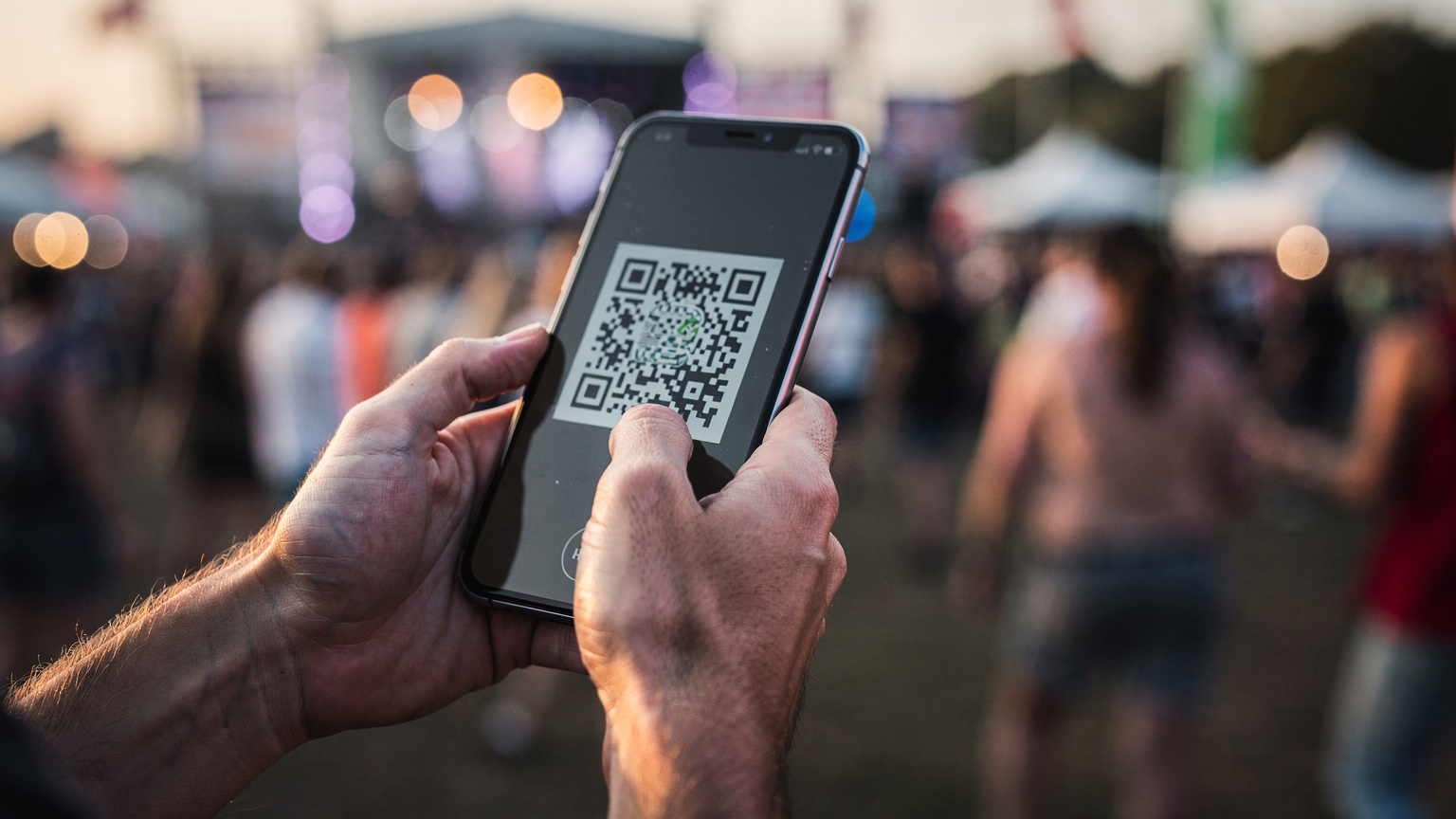 Bir festival katılımcısı, telefonunun ekranından gelen QR kodu tarayarak eSIM kurulumu yaparken, arka planda bulanık festival kalabalığı hareket ediyor.