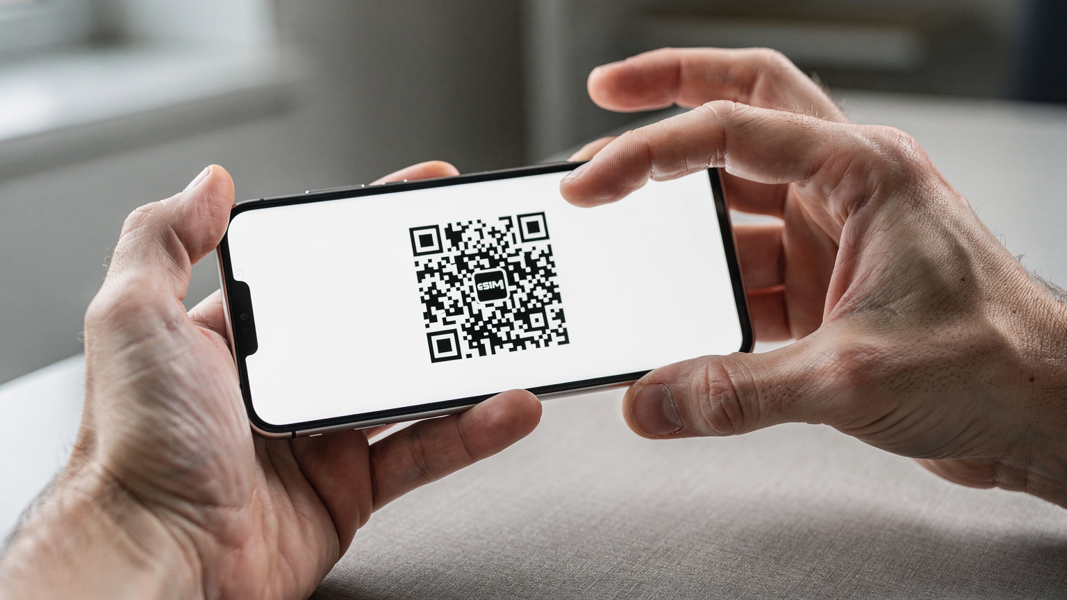 Two hands holding a smartphone, clearly displaying a QR code for eSIM installation against a soft, blurred background.