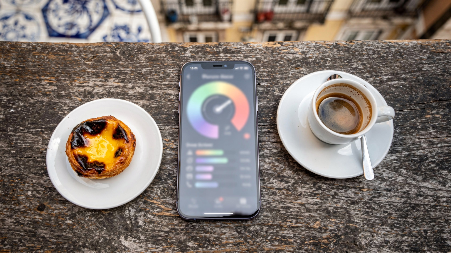 A close-up overhead shot of an iPhone displaying a Speedtest by Ookla result, resting on a rustic wooden table at an outdoor café in Lisbon, Portugal, with a pastel de nata and coffee nearby.