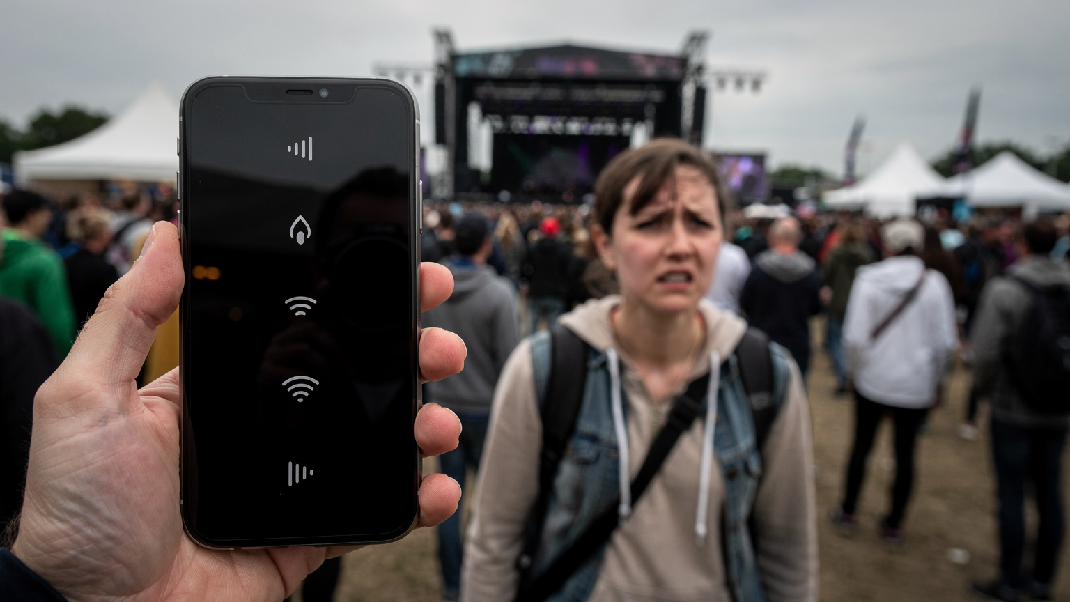 Ein Smartphone zeigt eine leere Netzwerkanzeige, während im Hintergrund ein Reisender mit besorgtem Gesichtsausdruck auf einem überfüllten Festivalgelände steht.