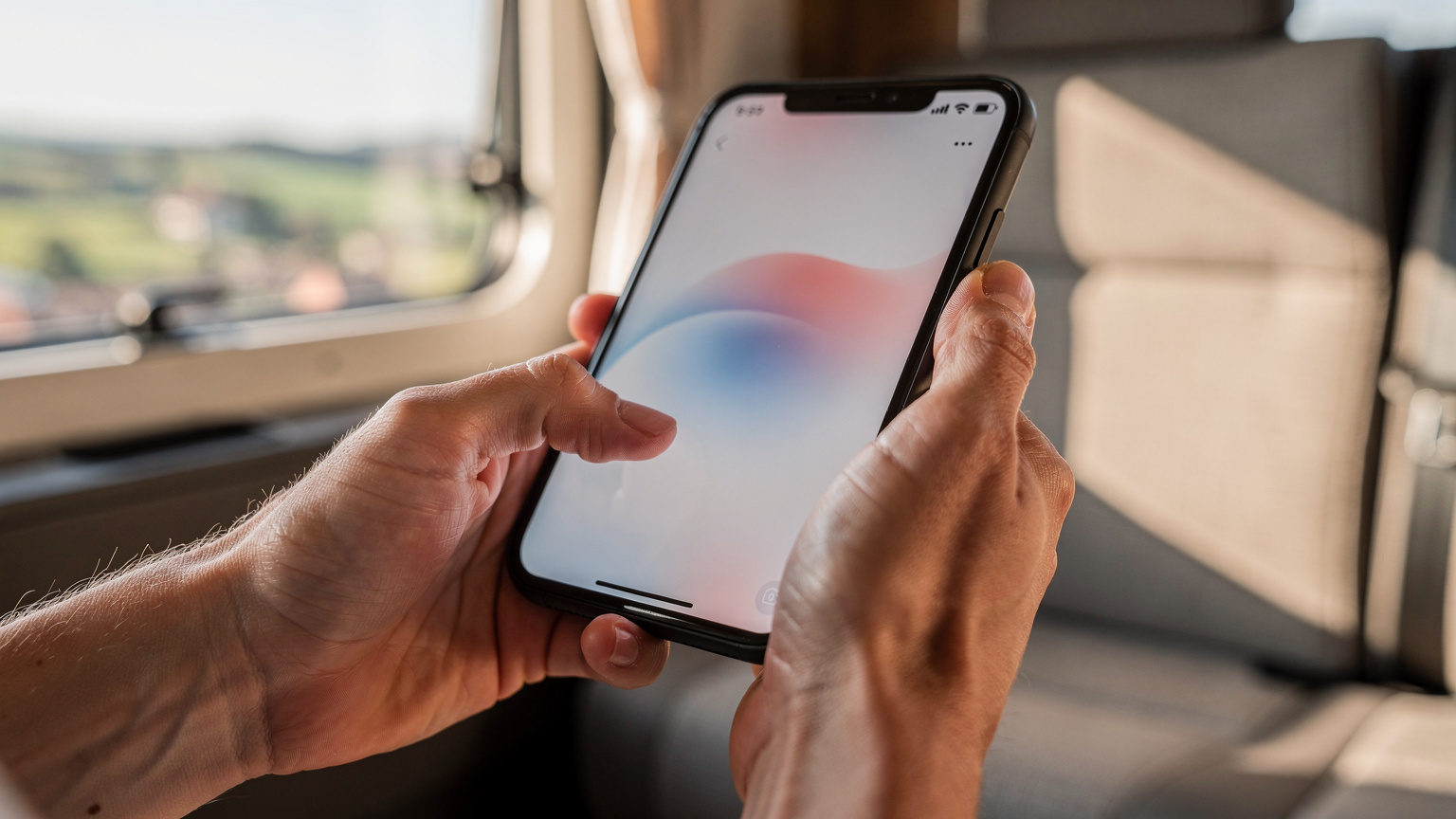 Een close-up van een paar handen in een camper, waarbij de duim een smartphone-scherm aanraakt om de mobiele data-instellingen te openen, met een onscherpe achtergrond van een landschap en camperinterieur.