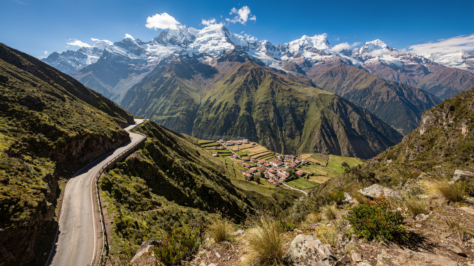 Uma vista panorâmica das montanhas dos Andes equatorianos, com uma estrada sinuosa e um pequeno vilarejo ao fundo, sugerindo a vasta geografia do país e a necessidade de conectividade fora das cidades.