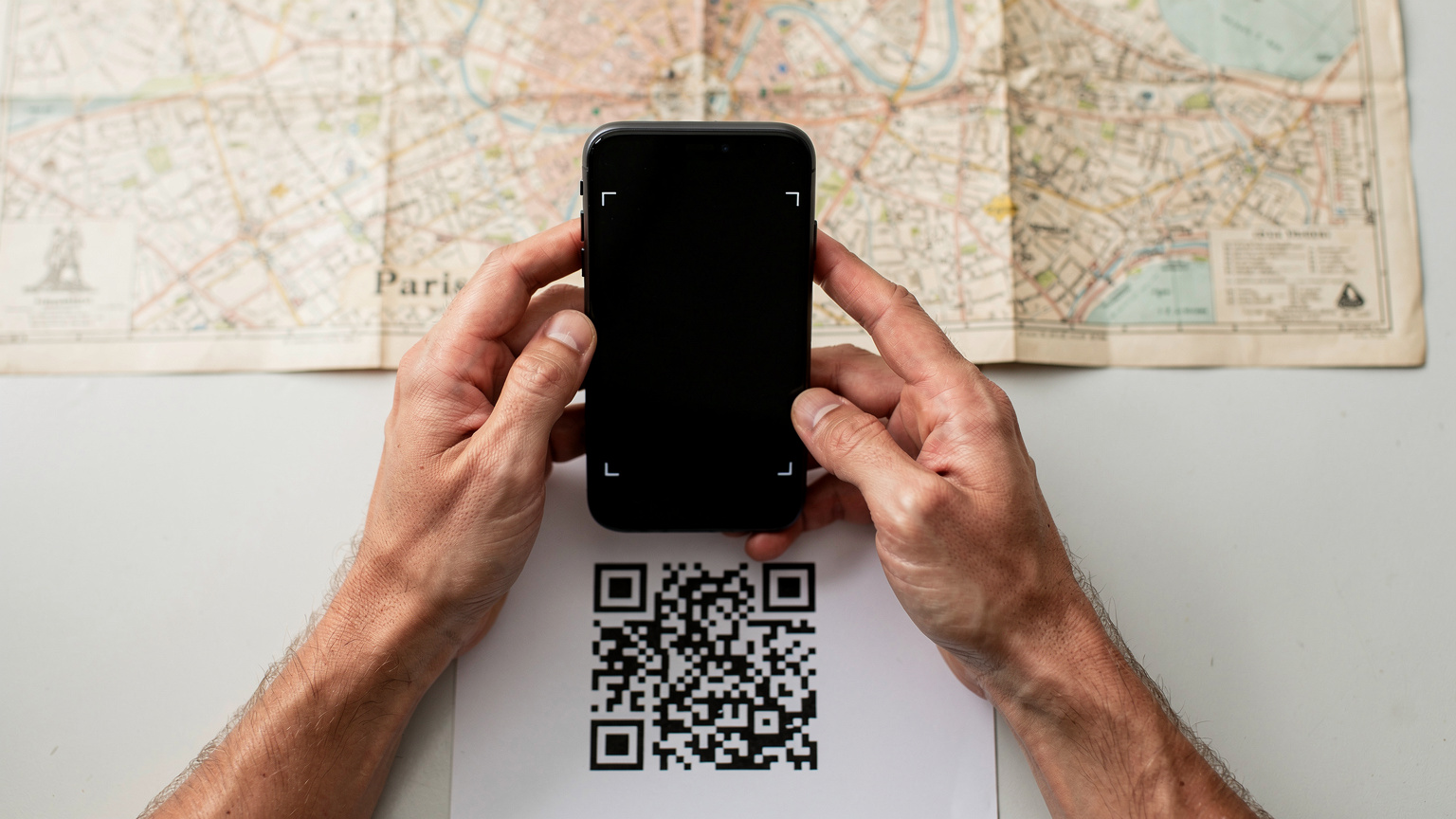Un gros plan sur des mains tenant un iPhone qui scanne un QR code pour activer une eSIM, avec une carte de Paris en arrière-plan, symbolisant la préparation d'un voyage.