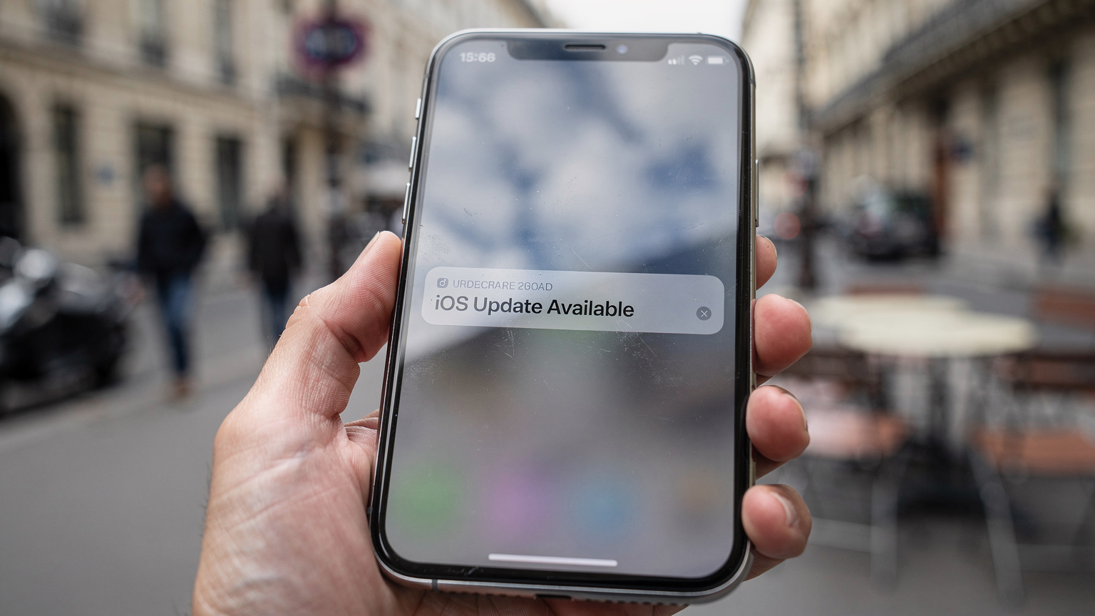 Un écran d'iPhone affichant la notification d'une mise à jour iOS disponible, avec un fond urbain flou suggérant la nécessité d'une bonne préparation avant un transfert d'eSIM.