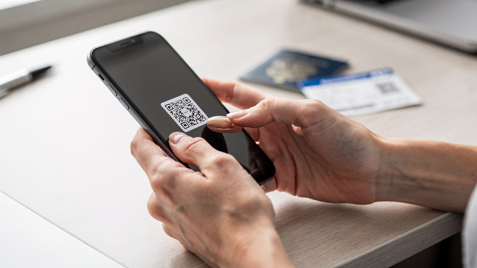 A woman's hands hold a smartphone, scanning a QR code for eSIM activation, with a blurred passport and boarding pass in the background.