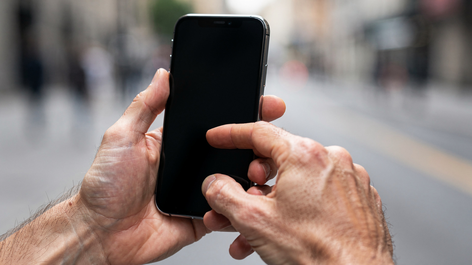 Mãos de uma pessoa segurando um smartphone moderno, com o polegar tocando a tela para navegar, em um fundo desfocado de uma paisagem urbana, ilustrando a facilidade de ativação de um eSIM com poucos toques.