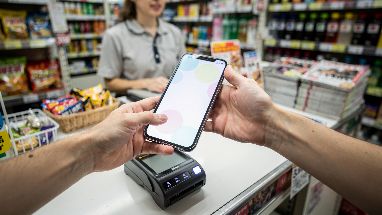 一位旅客在日本便利店的收銀台前使用手機支付,周圍是琳瑯滿目的商品。