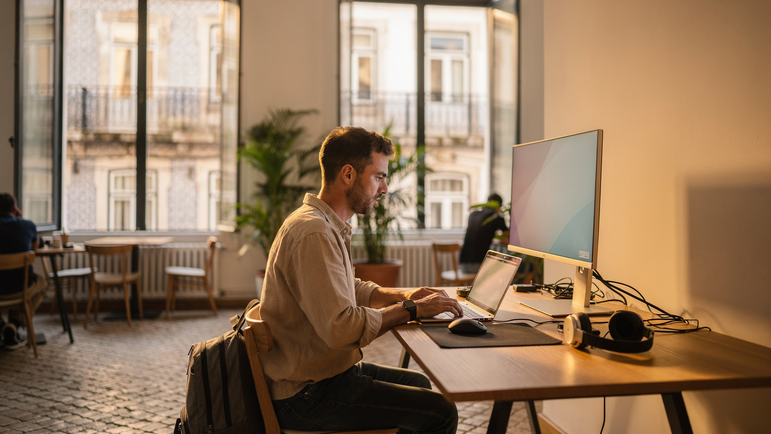 A traveler using a laptop with an external monitor in a minimalist co-working space in Lisbon, Portugal, illustrating the seamless integration of eSIMs with remote work setups.