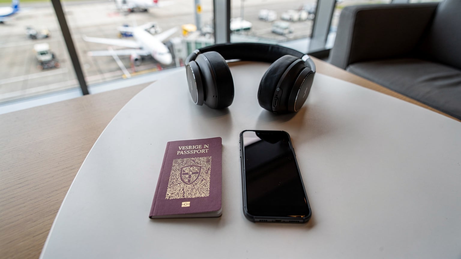 En bild som visar en resenärs passport och smartphone på ett kafébord, med en suddig bakgrund av en modern, teknikfylld flygplats lounge, symboliserande global uppkoppling.