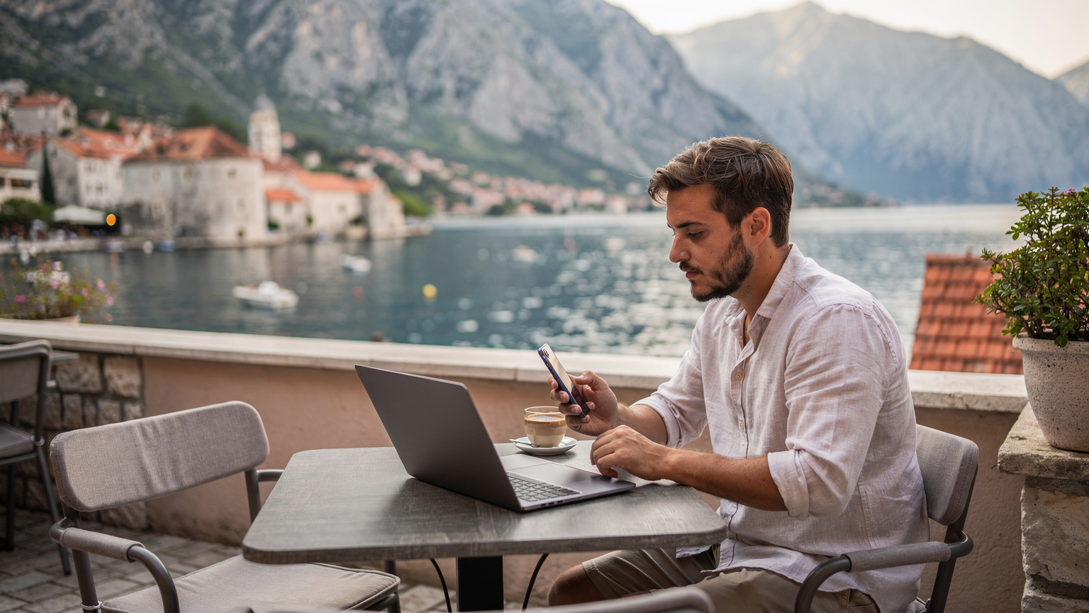 Kotor Körfezi'ne bakan bir kafede, dizüstü bilgisayarında ve telefonunda internet hızını test eden bir gezgin.